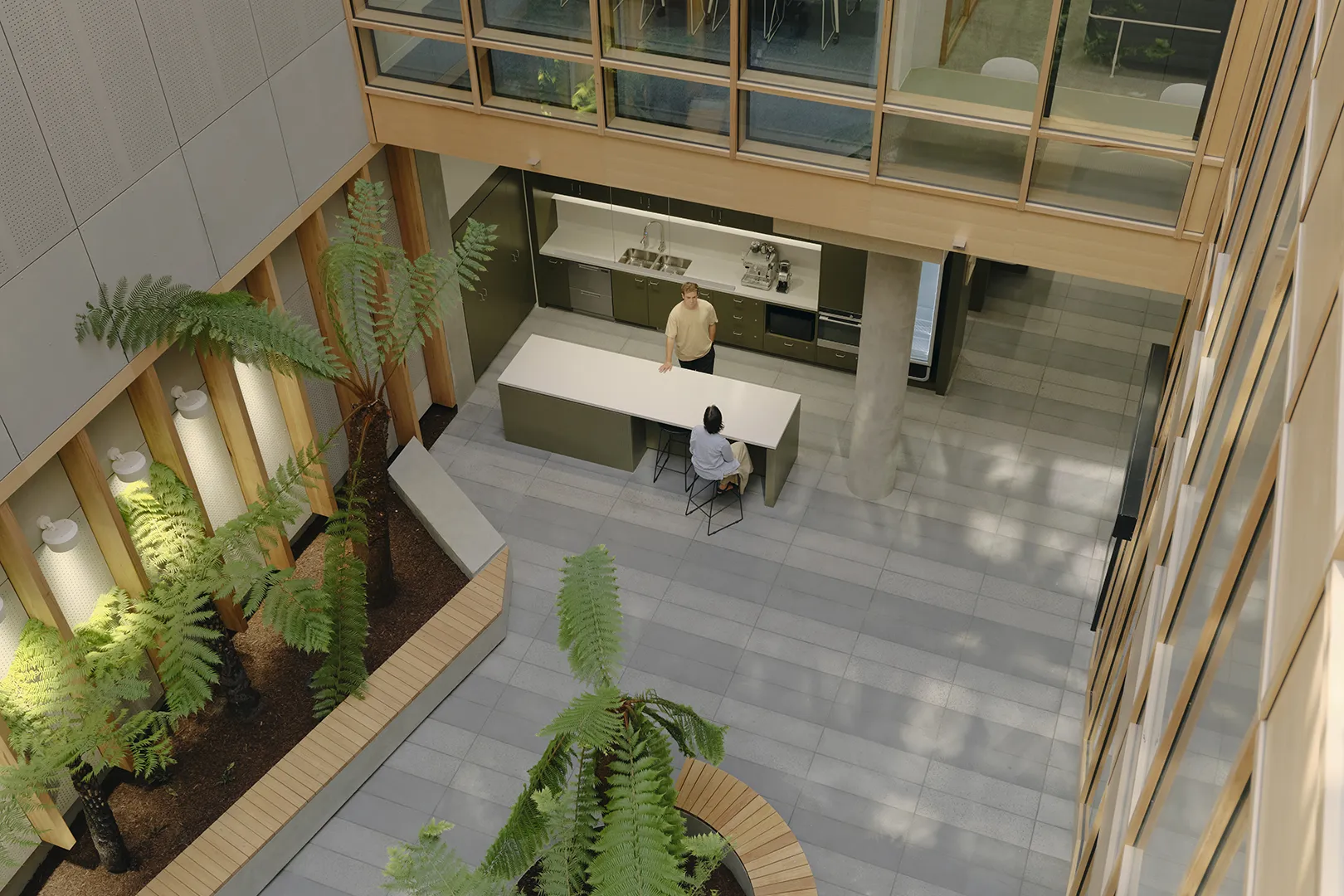 Open indoor atrium with seating, indoor planting, and shared kitchen facilities arranged around a central gathering space.