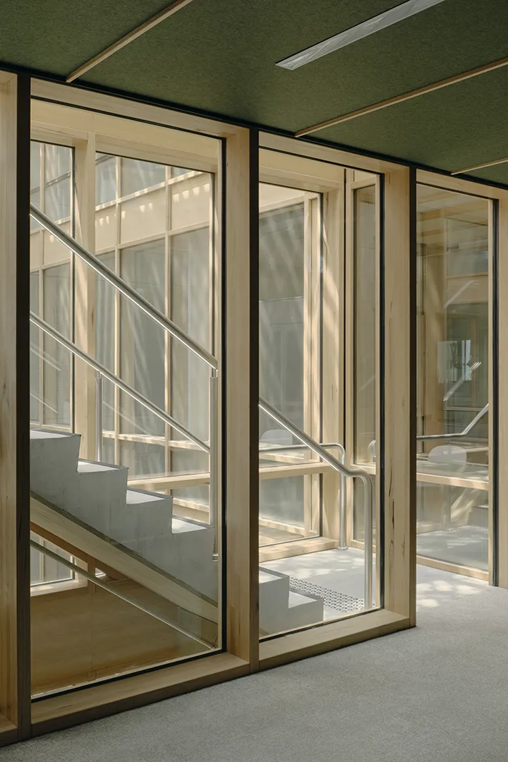 Internal walkway with floor-to-ceiling windows, timber framing, and views across the building's central atrium.