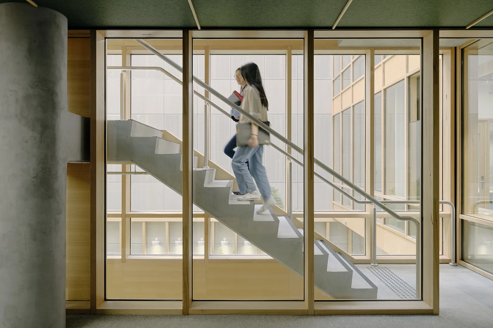 Student using a staircase within a light-filled interior featuring large windows and views across the central atrium.