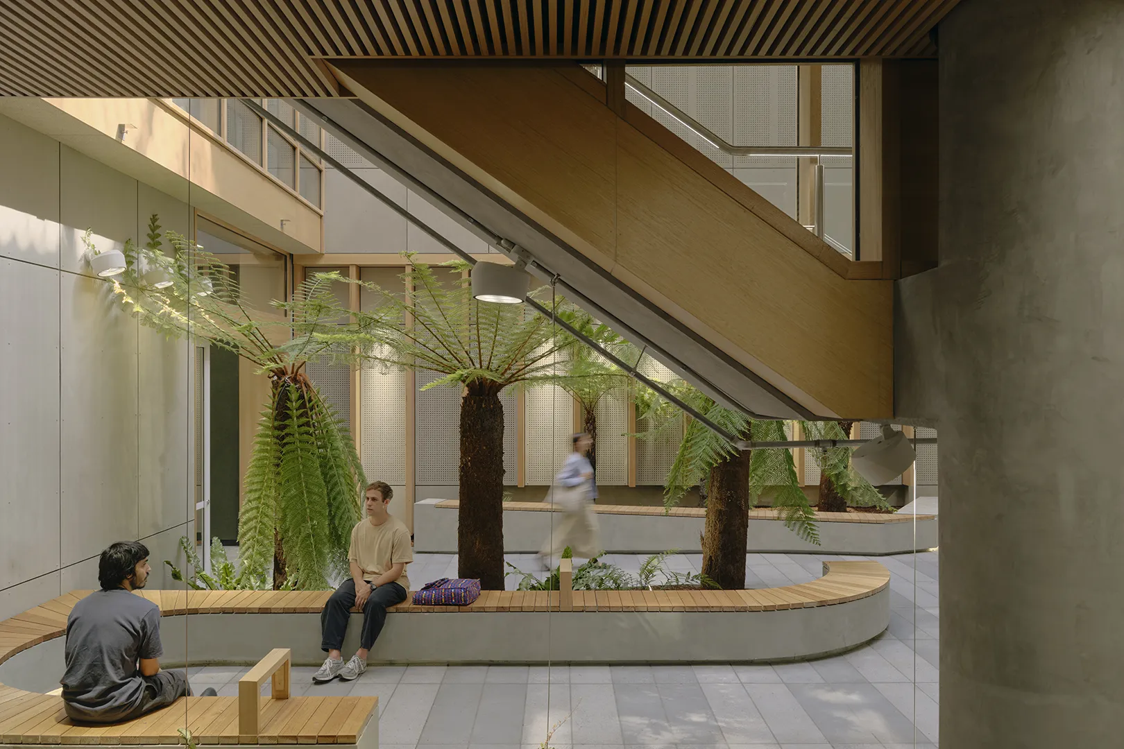 Students using seating areas within a central atrium featuring indoor planting, natural light, and open circulation spaces.