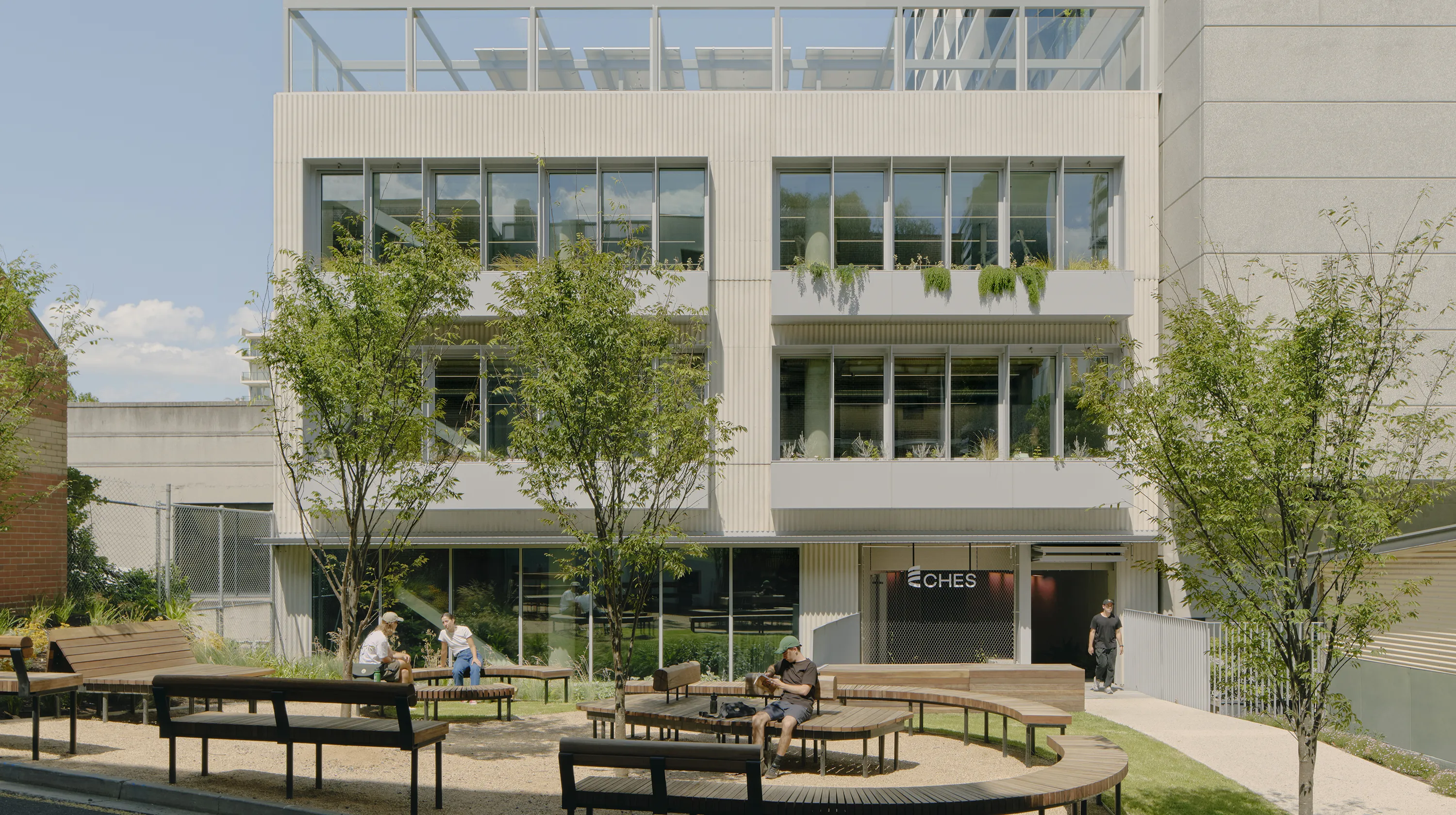 Centre for Higher Education Studies building with landscaped outdoor seating, mature trees, and large windows overlooking a shared courtyard.