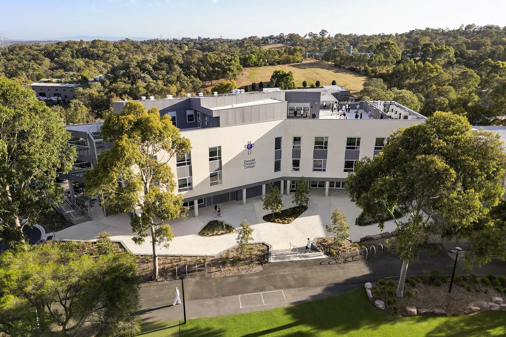 Aerial view of a school building set within landscaped grounds, open courtyards, and surrounding bushland.