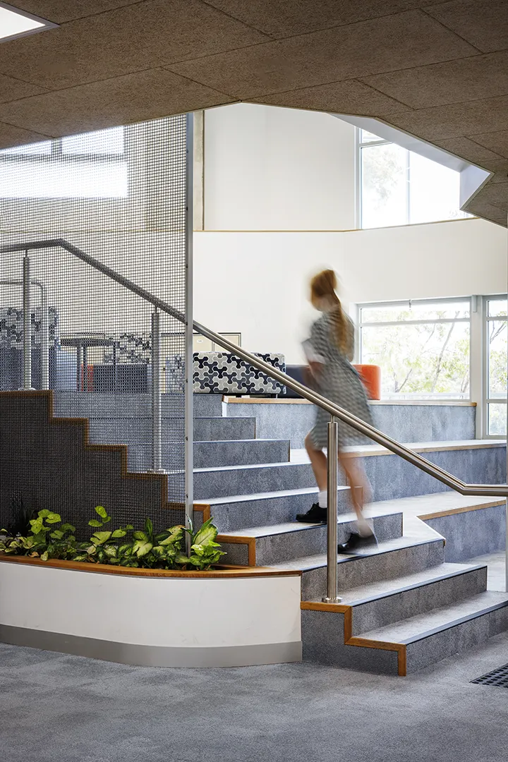 Student moving through a stepped learning space with integrated seating, indoor planting, and natural light.