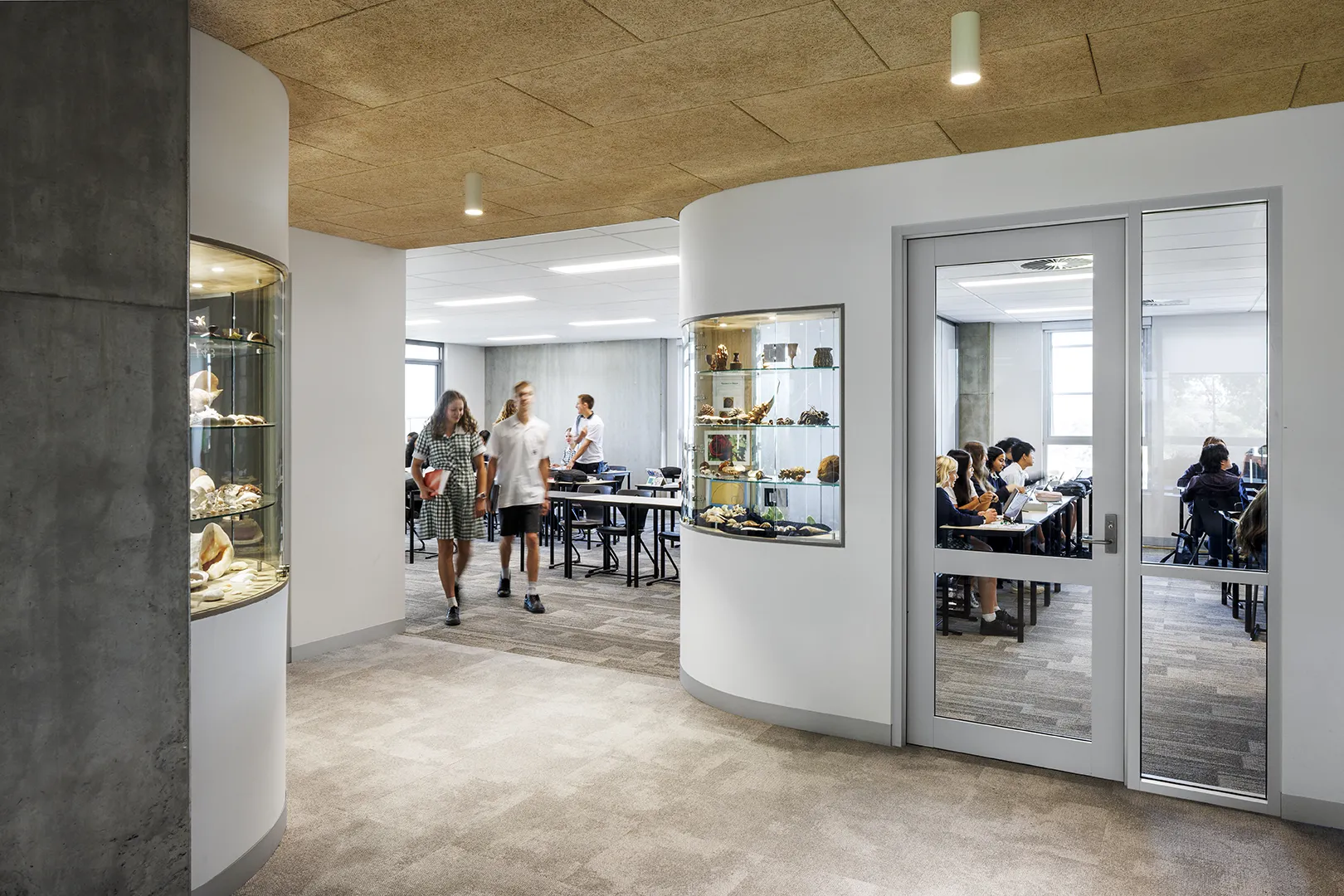 Students moving through a classroom area with display cabinets, flexible learning spaces, and adjoining study rooms.