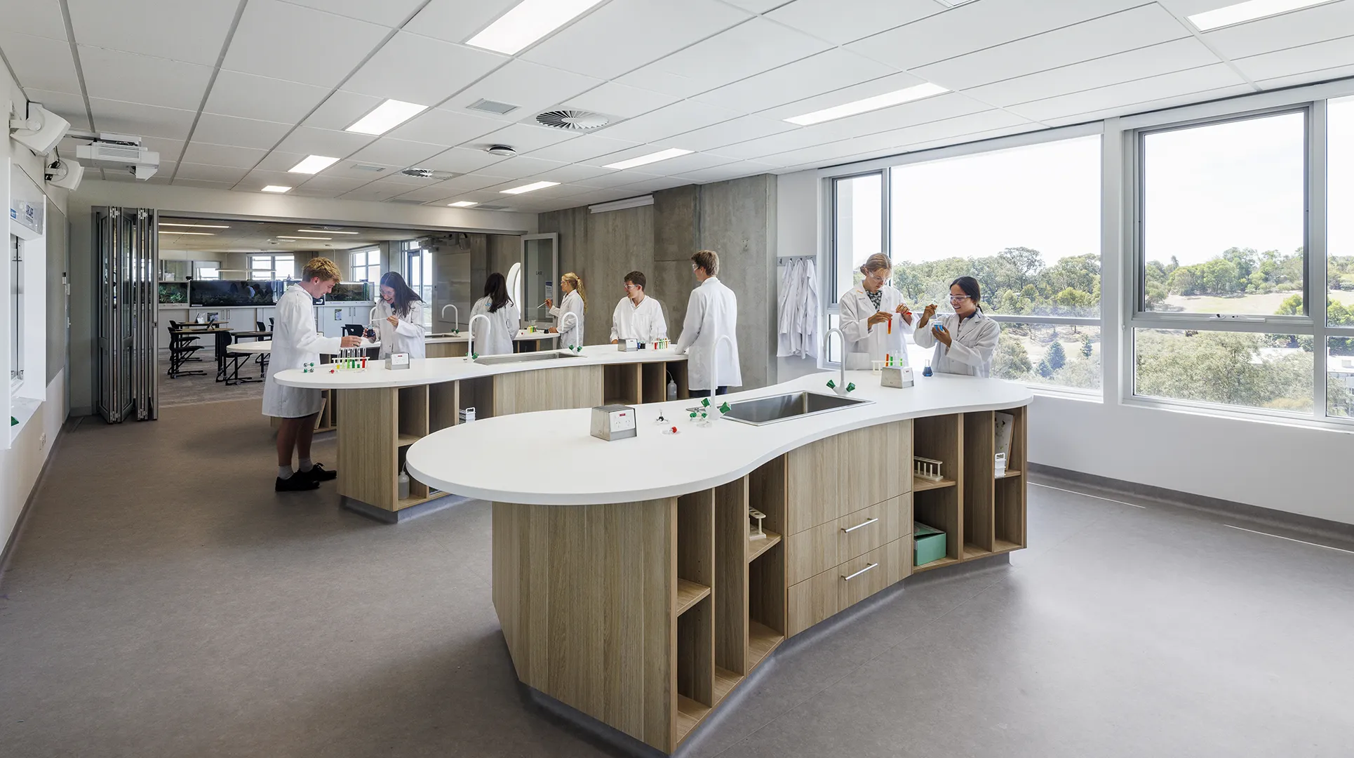 Students conducting experiments in a science laboratory with practical workstations and large windows overlooking the campus.