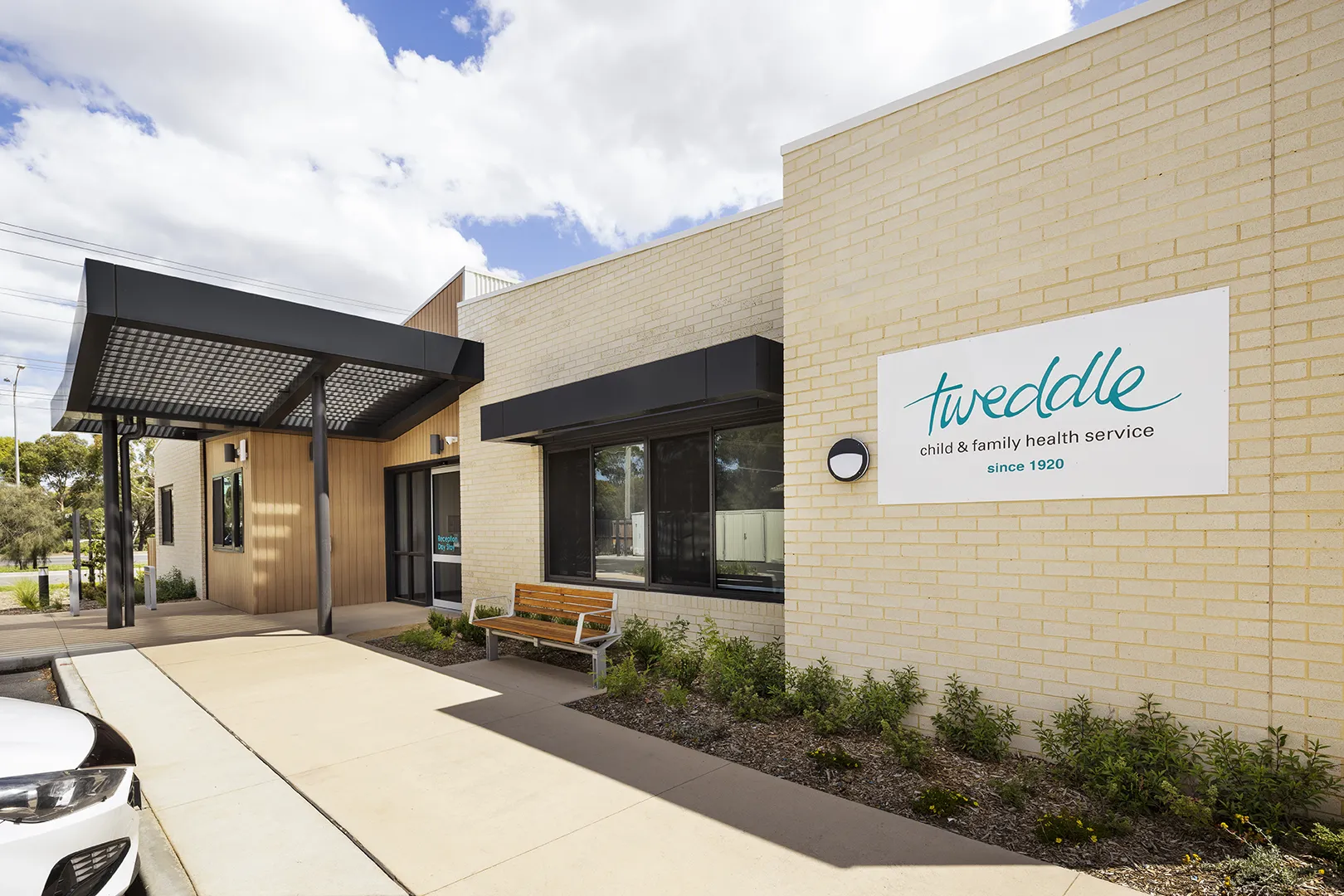 Main entrance to the centre with covered access, seating, landscaped gardens, and clear visitor signage.