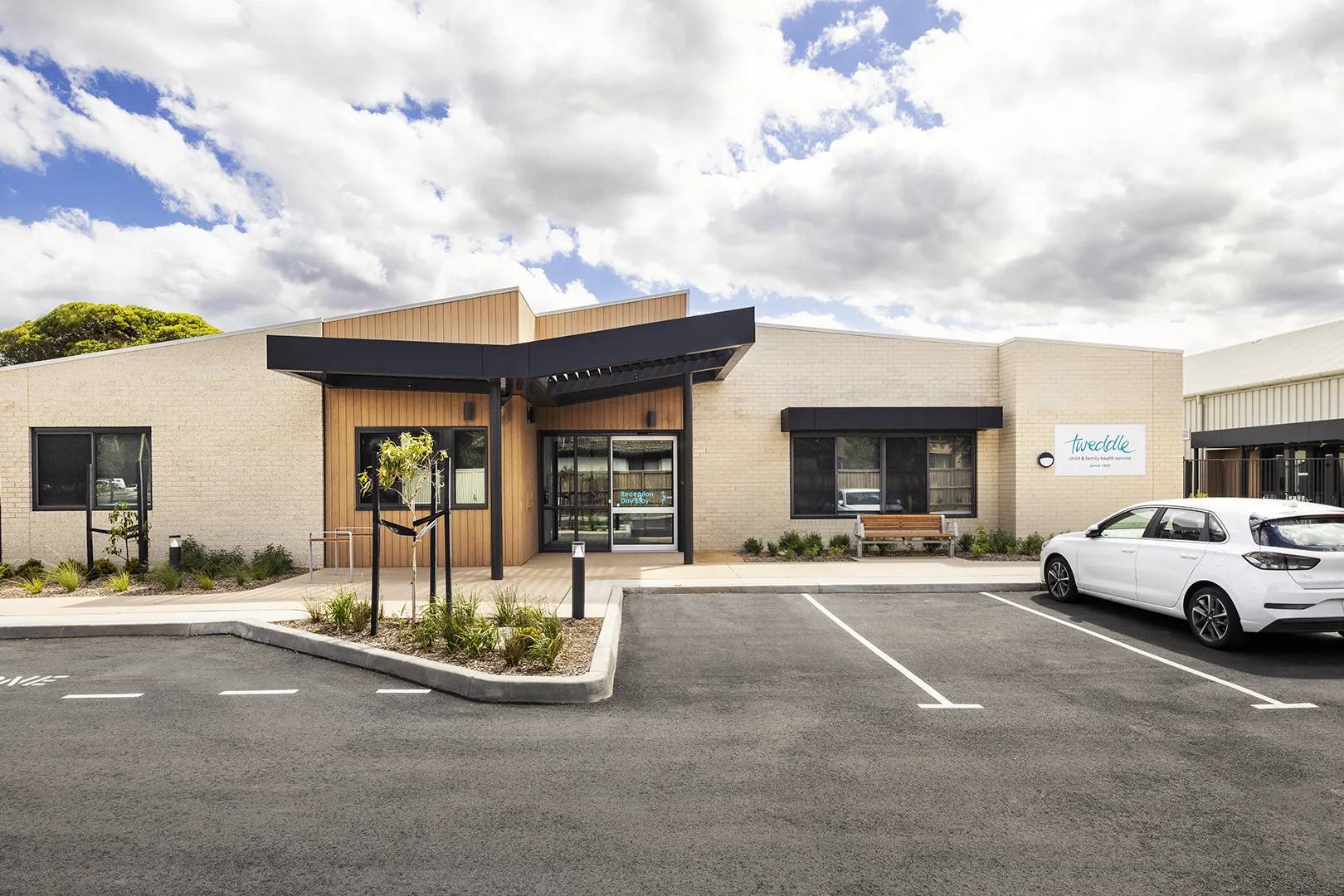 Exterior view of the centre with a covered entrance, accessible pathways, landscaped gardens, and visitor parking.