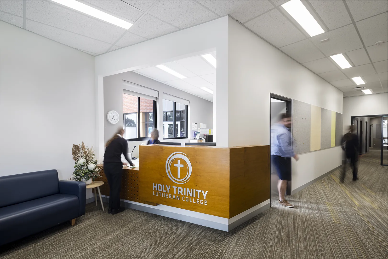 Reception area with a welcome desk, visitor seating, and staff assisting people at the college entrance.