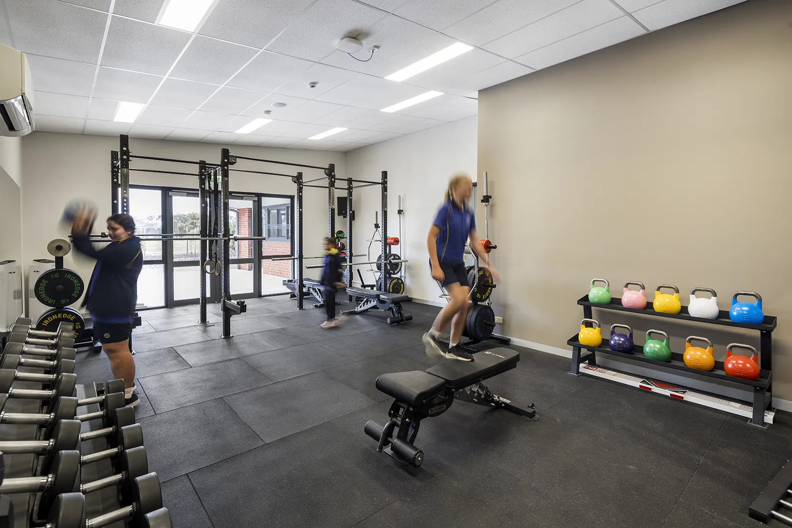 Students using a fitness and training space equipped with weights, exercise equipment, and areas for physical education.