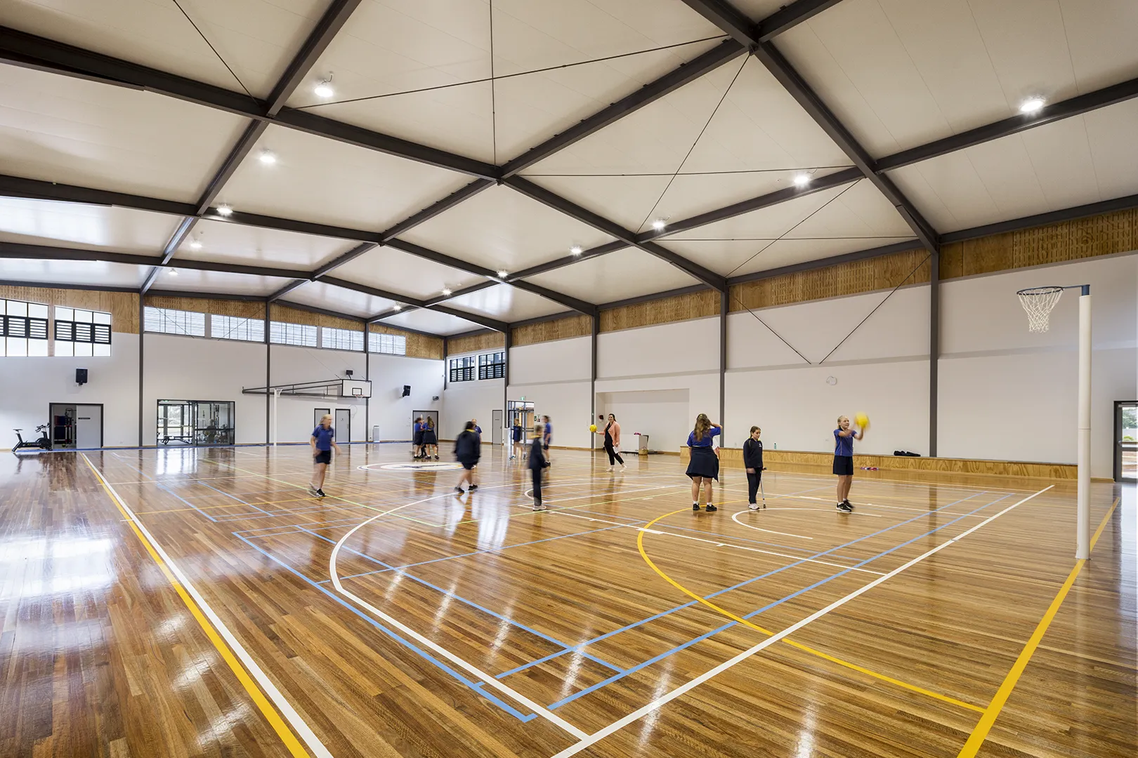 Students participating in indoor sports and physical activities in a large multi-purpose gymnasium.