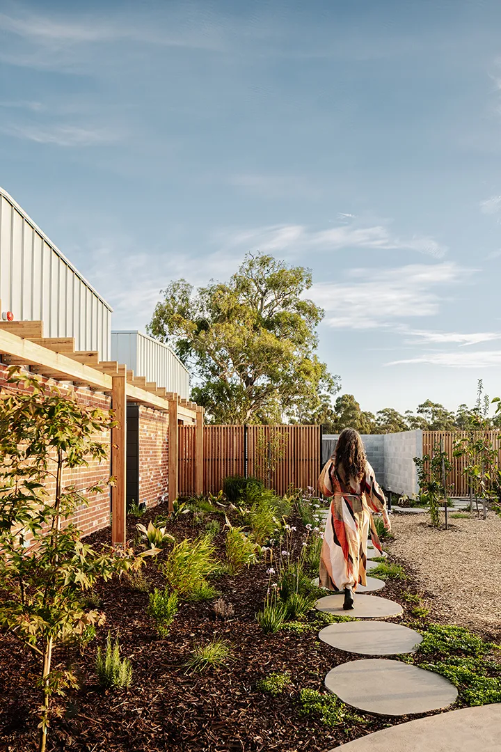 Person walking through a landscaped garden with pathways, planting, and private outdoor spaces for residents.