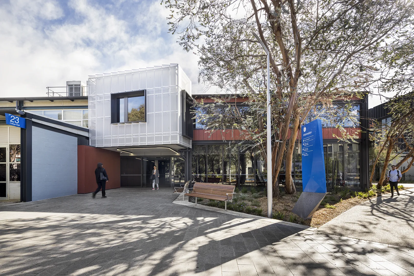 Campus building entrance with outdoor seating, mature trees, and pathways connecting learning and research spaces.