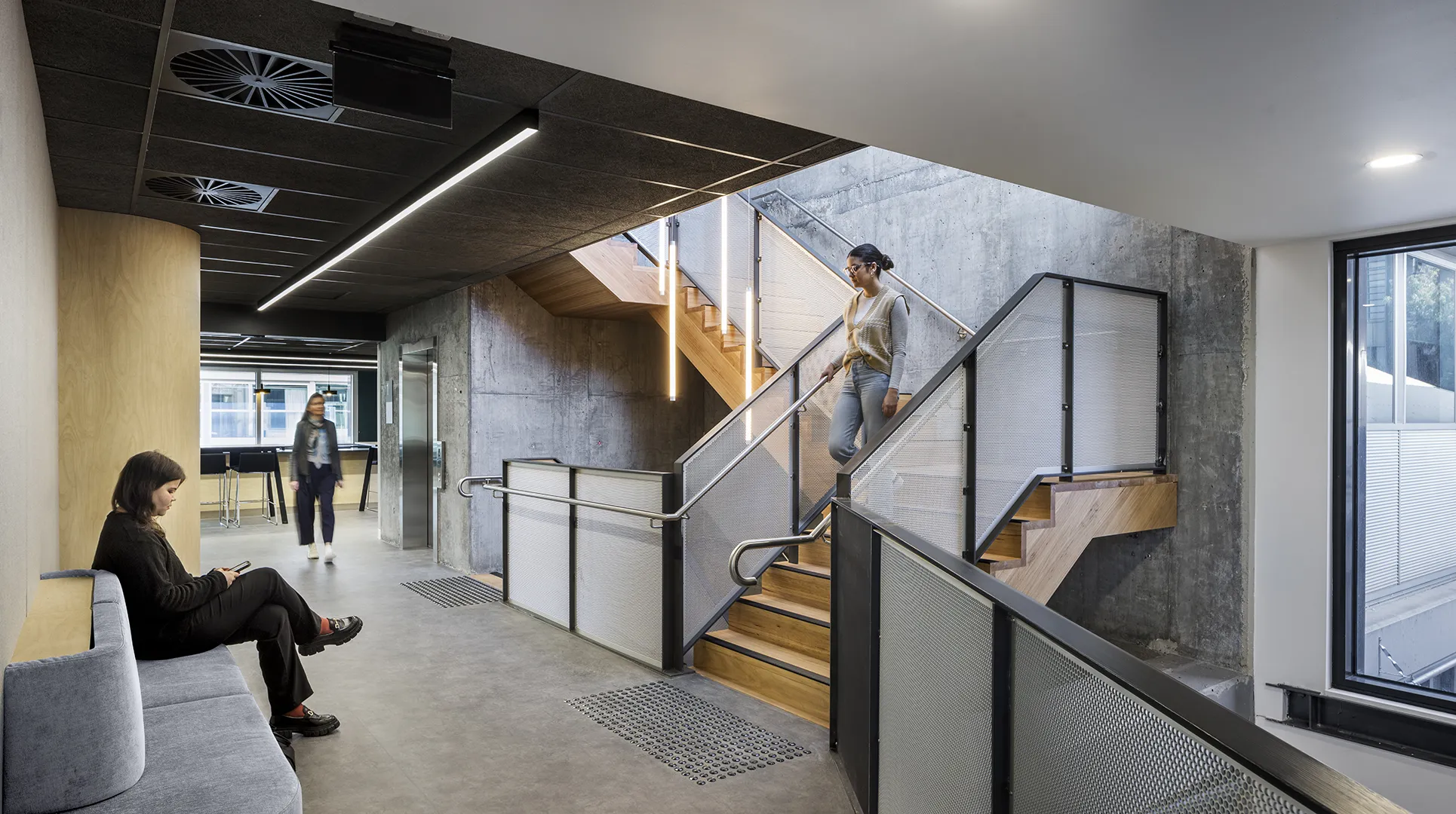 People moving through an open interior with stair access, informal seating, and spaces for study and collaboration.