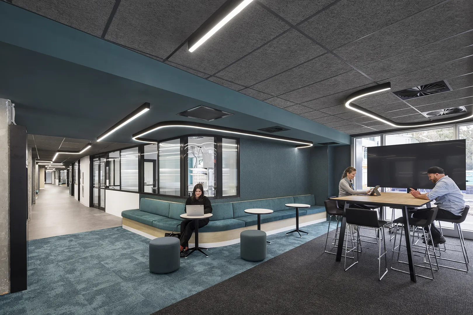 People working and meeting in a collaborative study area with flexible seating, tables, and adjoining learning spaces.