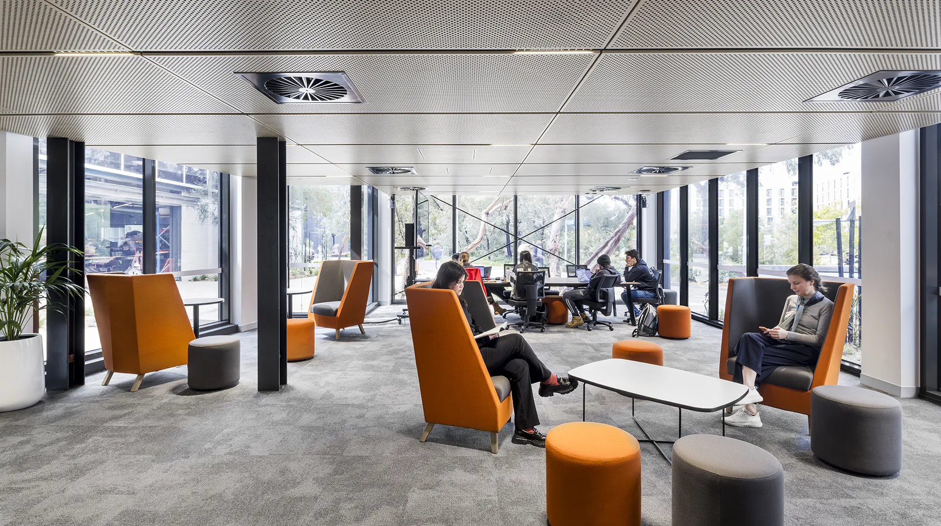 People using a quiet study lounge with comfortable seating, work areas, and large windows overlooking the campus.