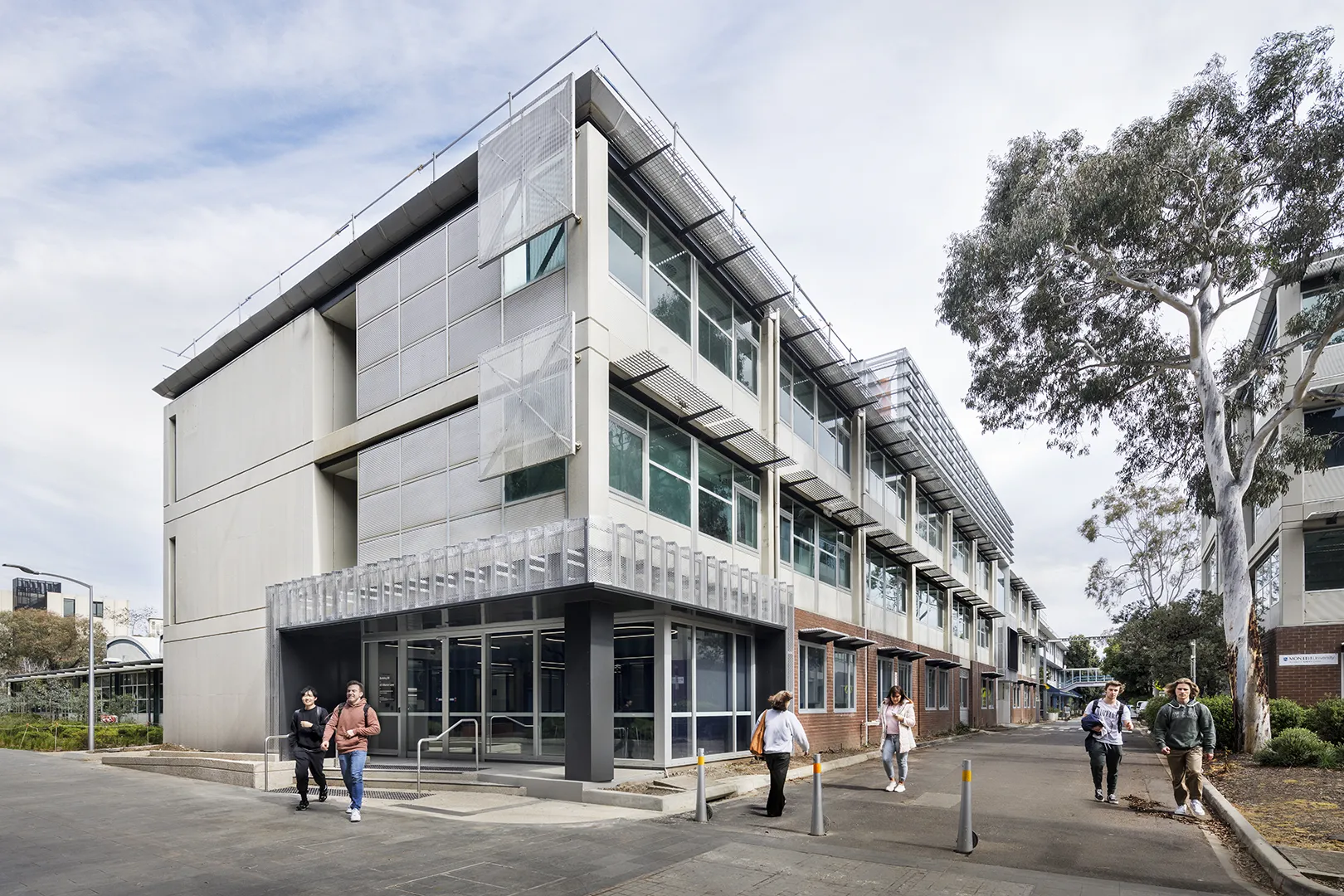 University building exterior with pedestrian pathways, large windows, and people moving through the campus.