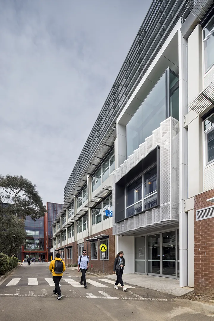 University building exterior with pedestrian pathways, large windows, and people moving through the campus.