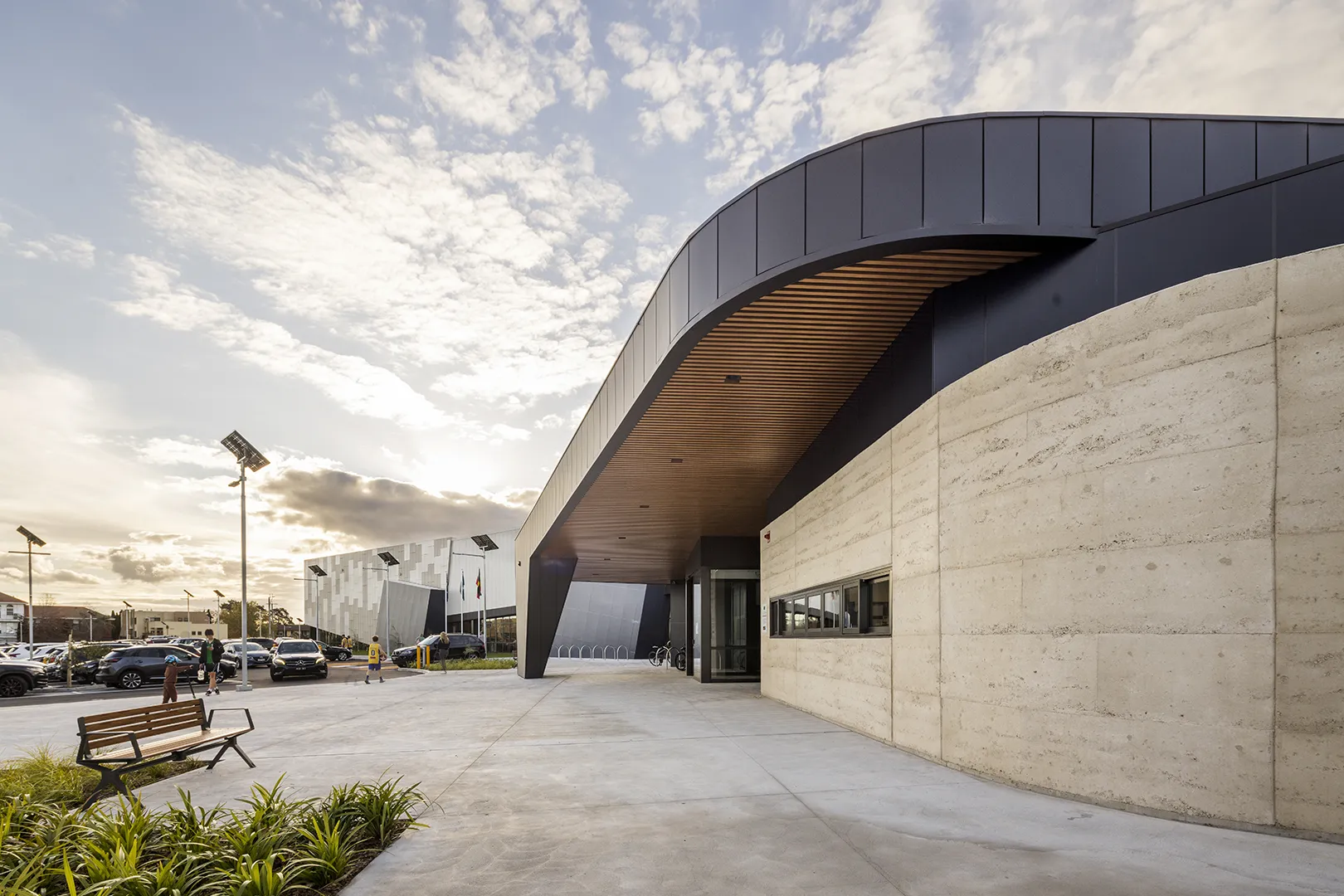 Covered entrance walkway with seating, landscaped planting, and pedestrian access to the stadium.