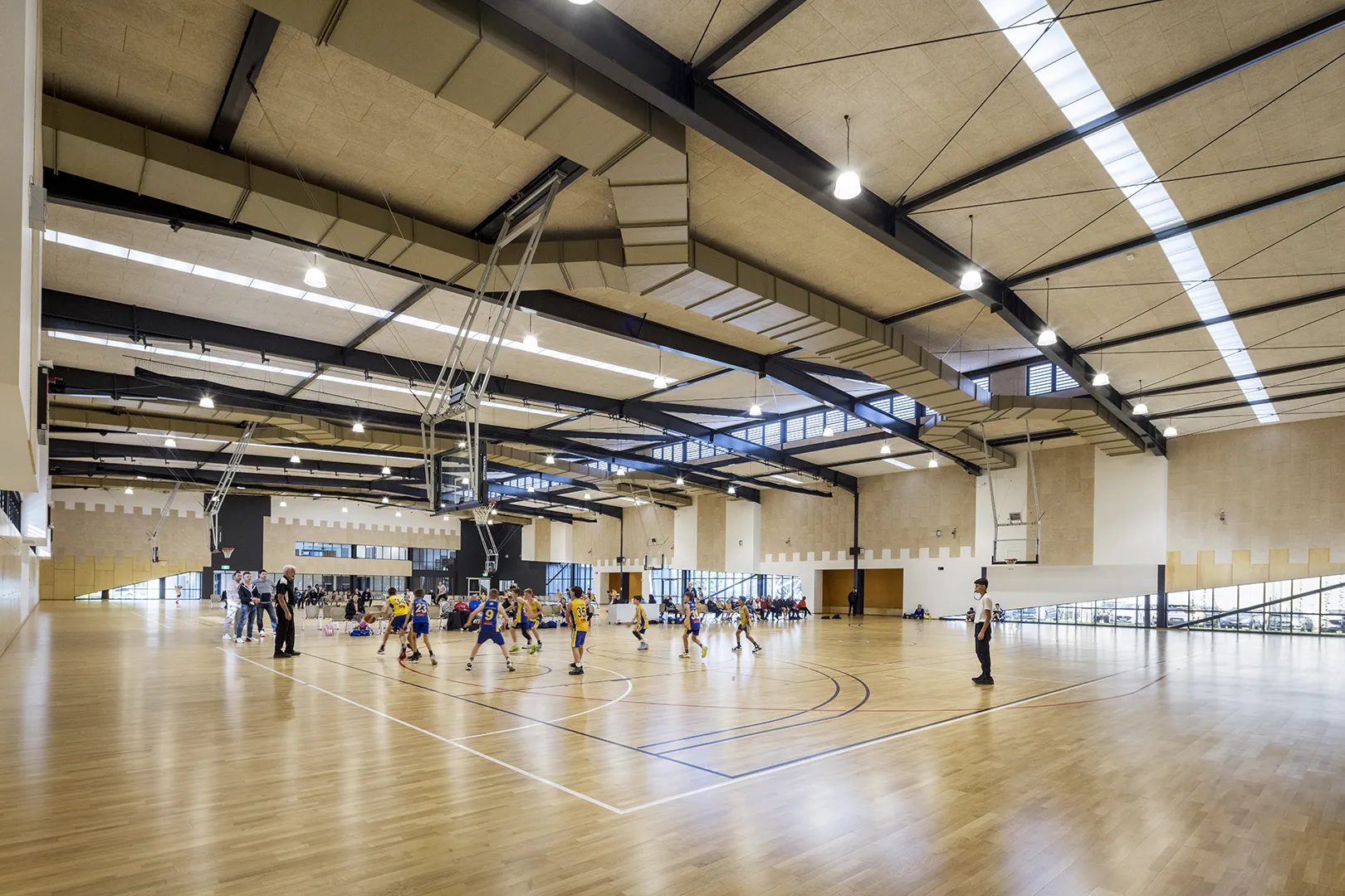 Large indoor sports hall with multiple basketball courts, spectator areas, and community sporting activities underway.