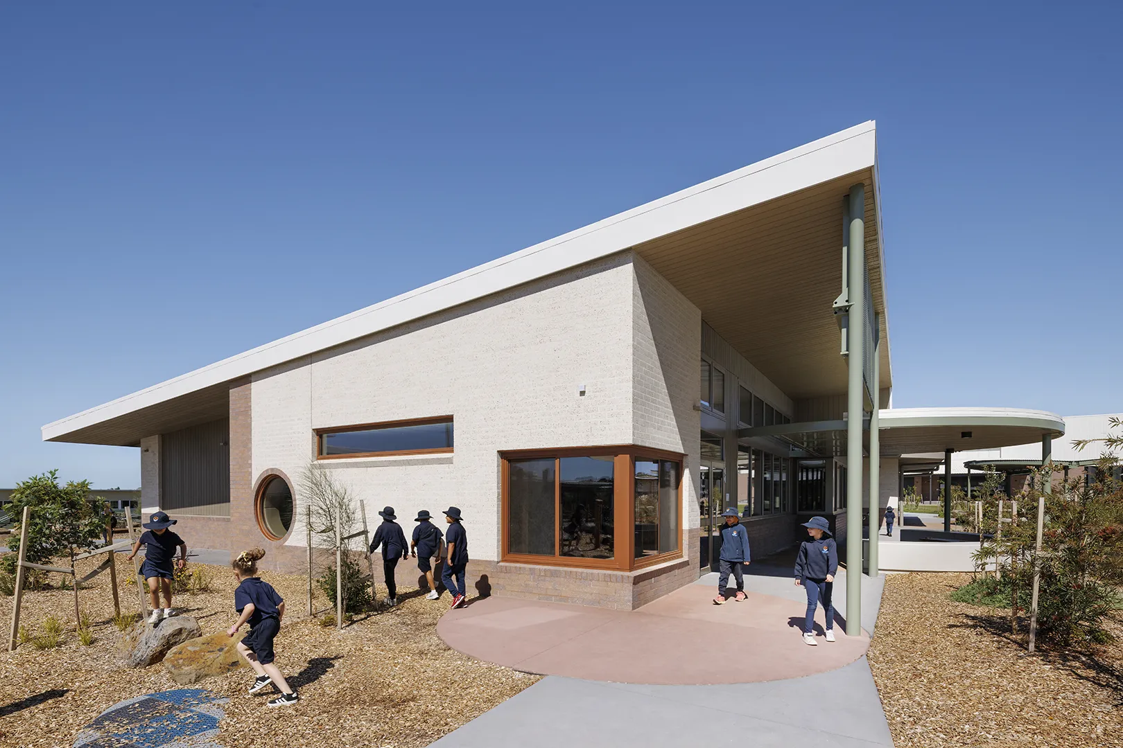 School building with large windows, covered walkways, and landscaped outdoor learning spaces.