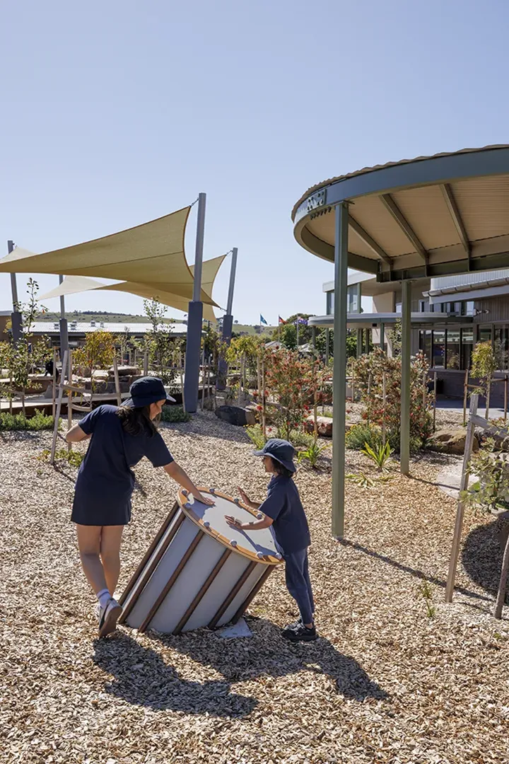 Children using an outdoor learning and play area with shade sails, gardens, and interactive play features.
