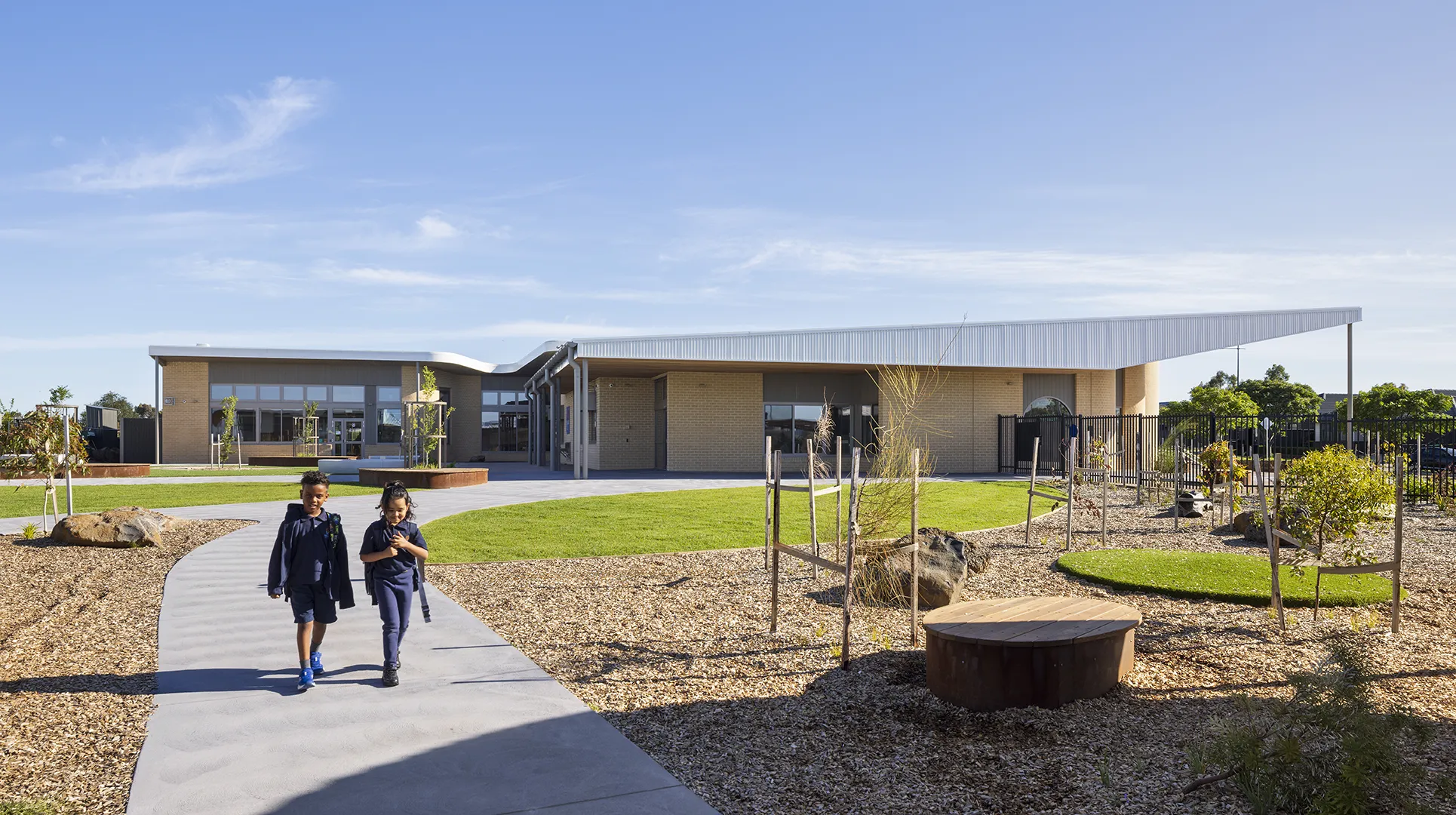 Two children walking along a pathway through landscaped school grounds with gardens and outdoor learning spaces.