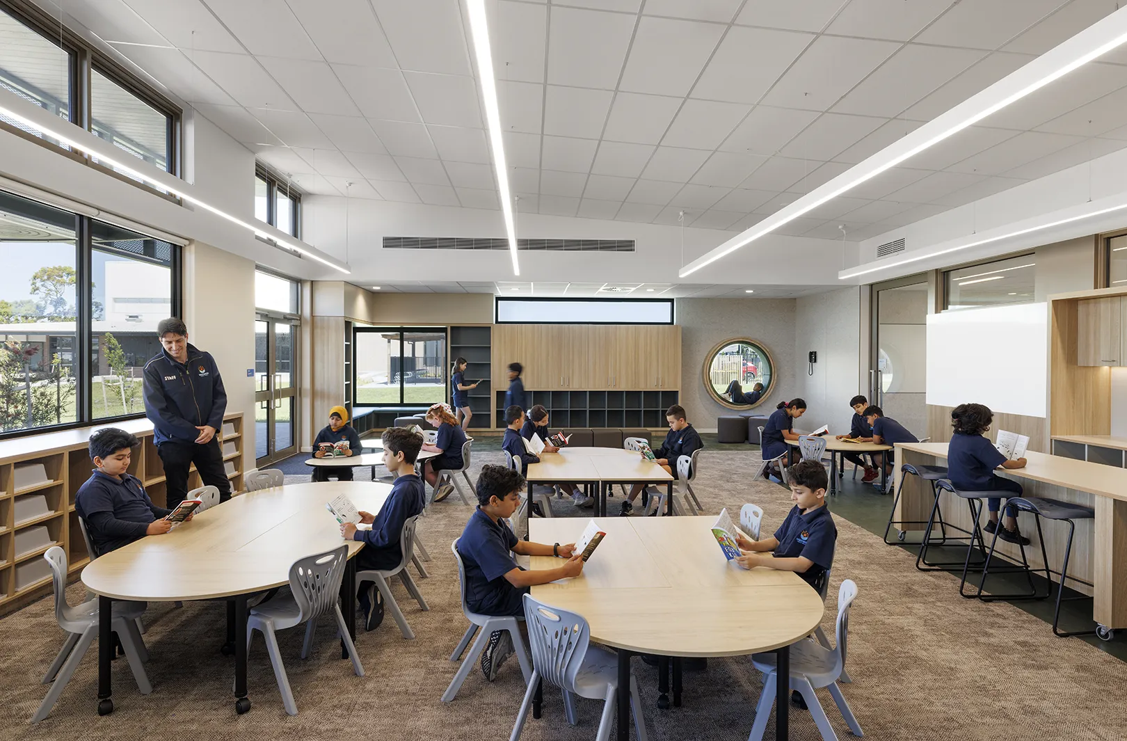 Students reading and learning in an open classroom with flexible seating, large windows, and built-in storage.