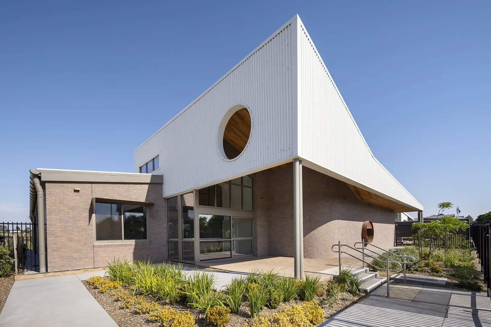 School building with a covered entrance, large windows, landscaped gardens, and accessible pathways.