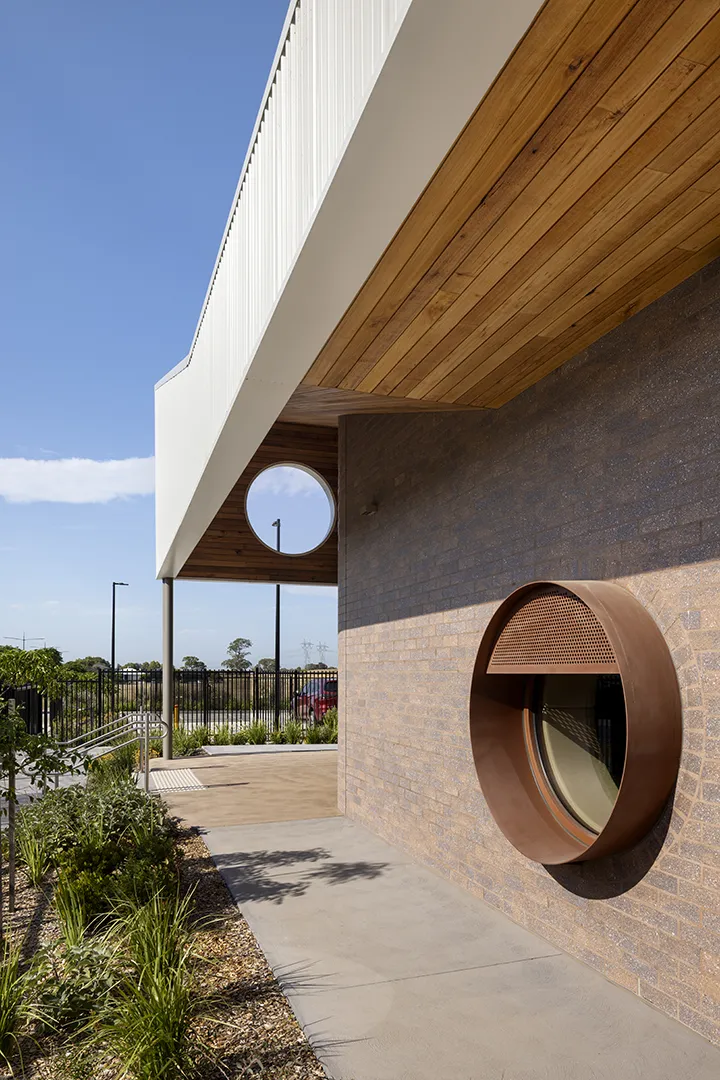 Covered walkway with landscaped gardens, a circular window, and distinctive exterior building details.