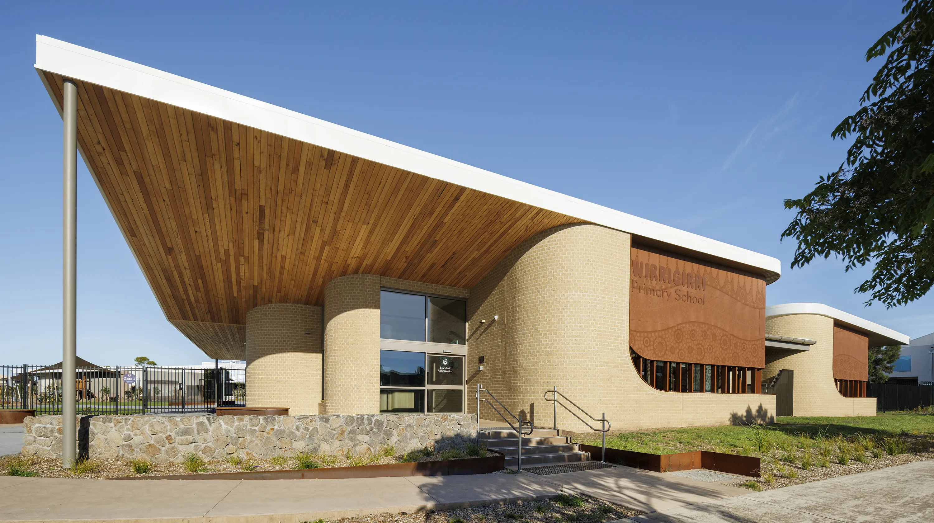 Main entrance of the school featuring a distinctive roof canopy, curved building forms, and landscaped outdoor areas.