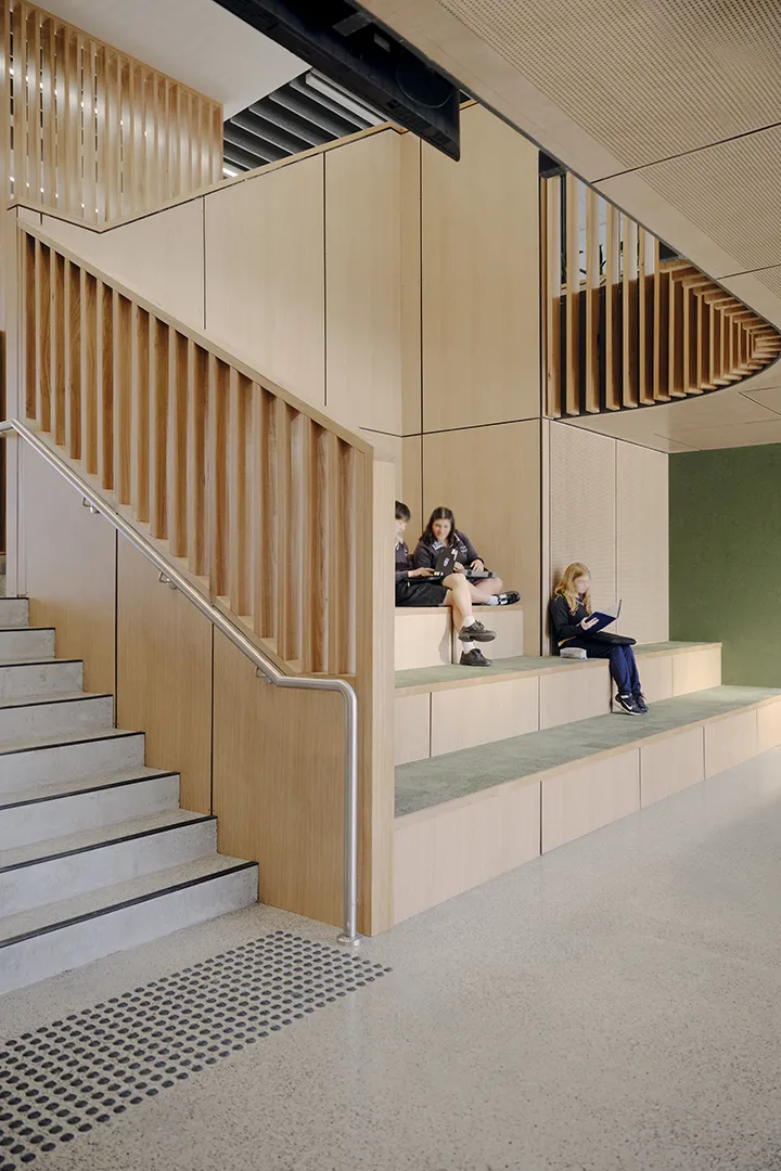 Students using tiered seating and informal study areas beside a staircase within a shared learning space.