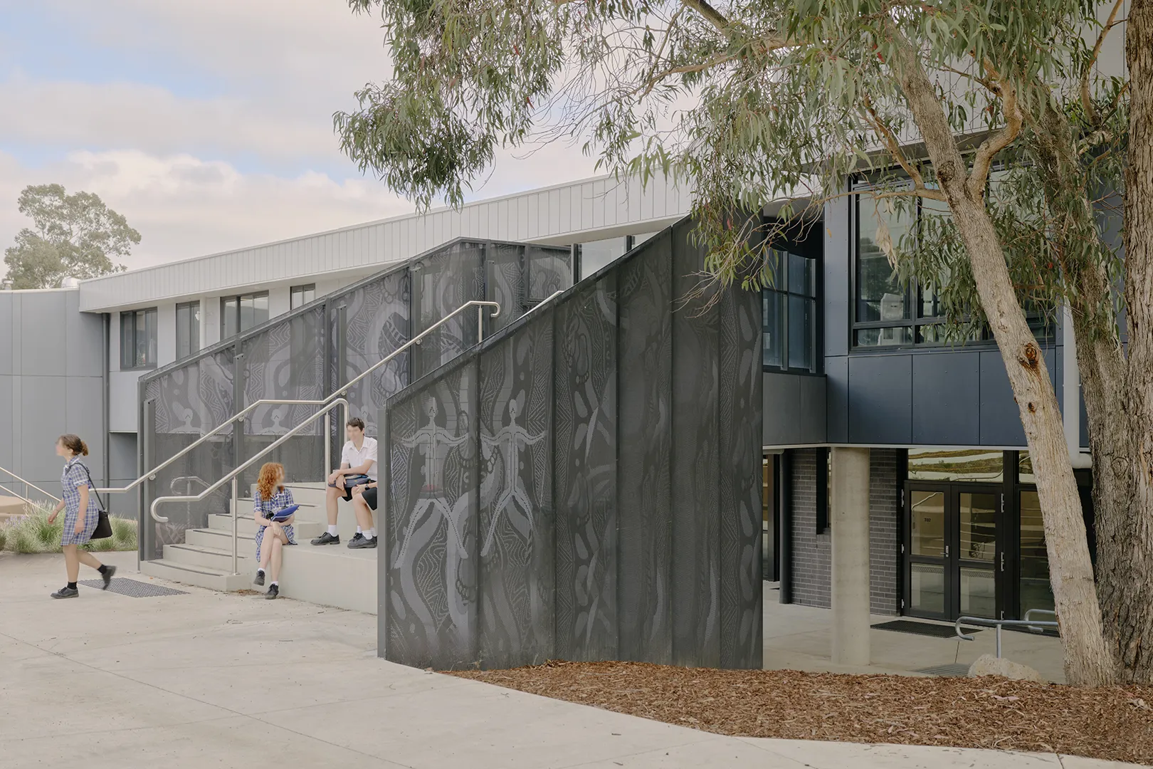Students using outdoor stairs and seating areas beside the STEAM Centre, with shaded walkways and landscaped surroundings.