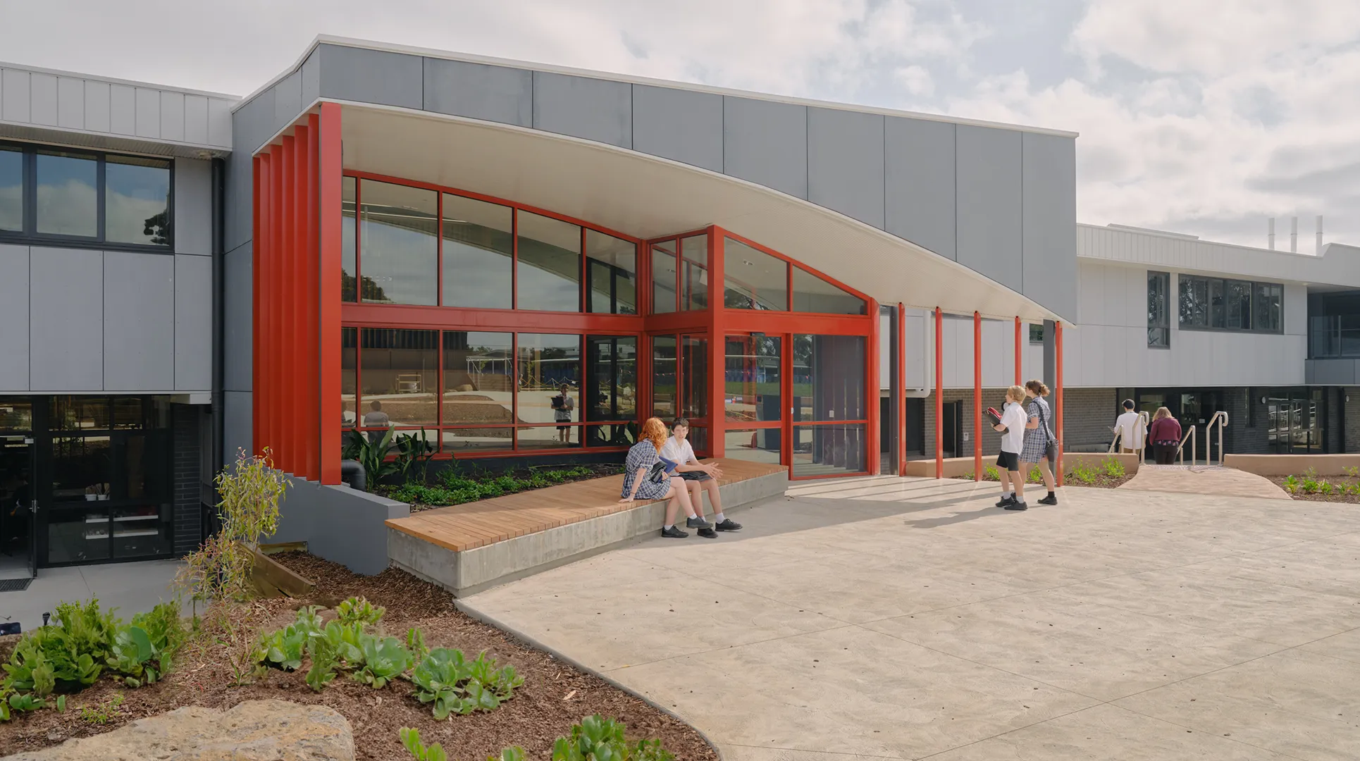 Students gathering outside the STEAM Centre entrance with outdoor seating, landscaped gardens, and open campus spaces.