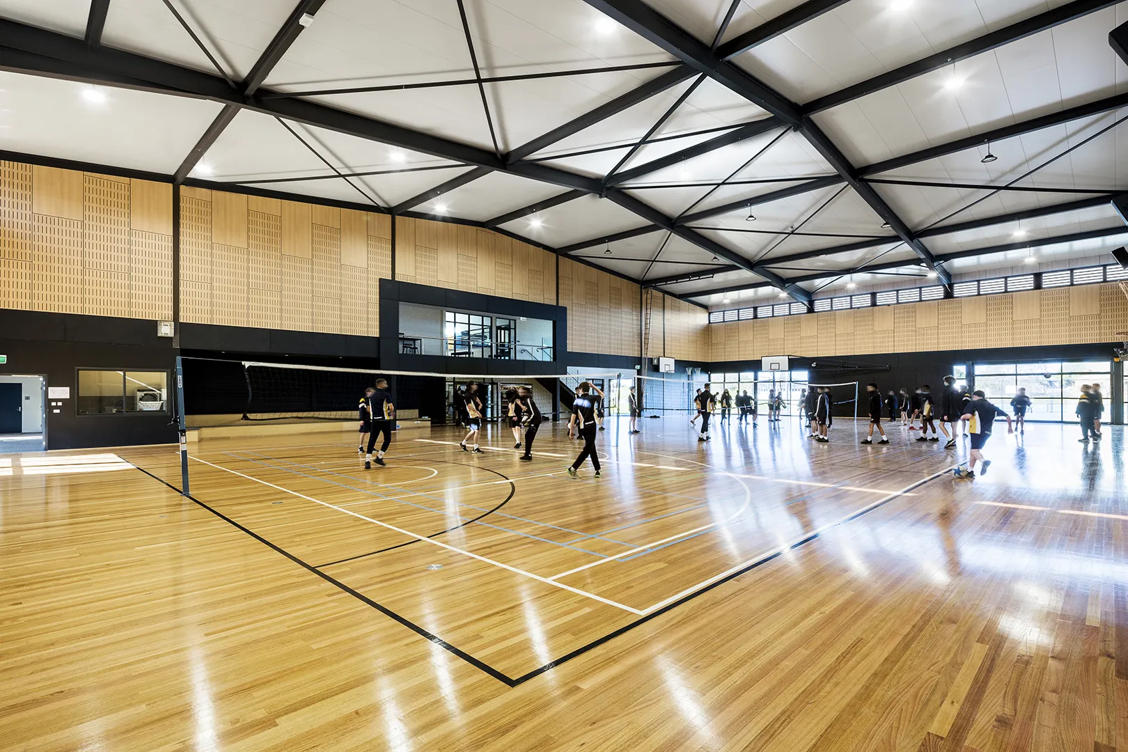 Students participating in indoor sports and physical education activities within a multi-purpose school sports hall.