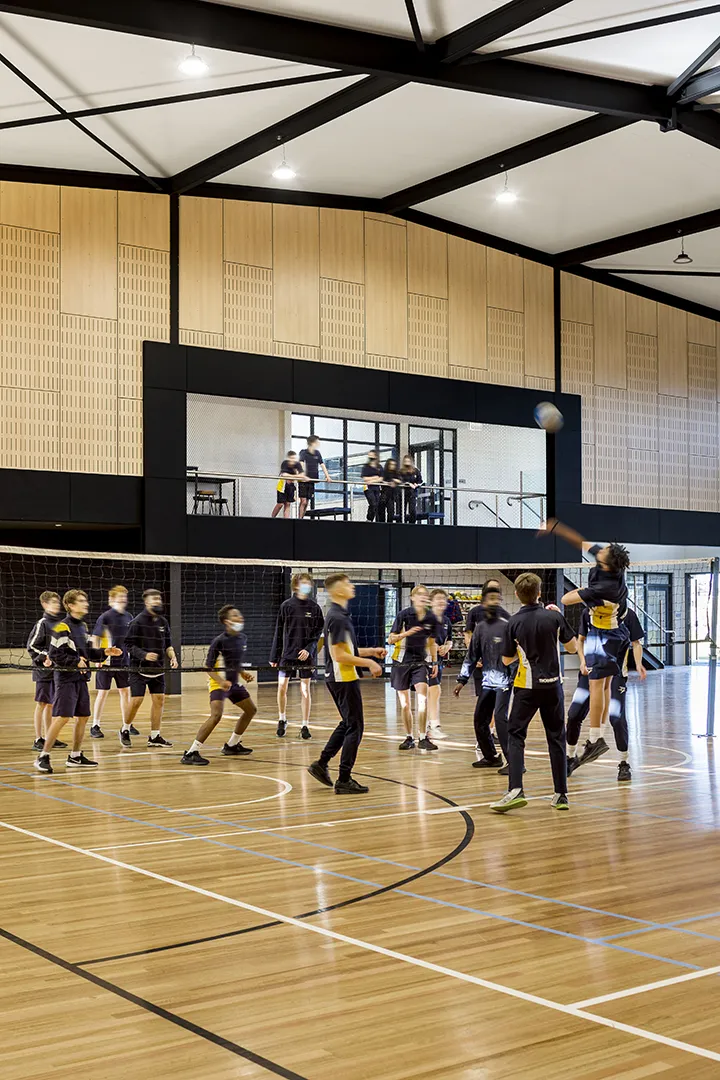 Students playing volleyball in an indoor sports hall with courts for physical education and community activities.