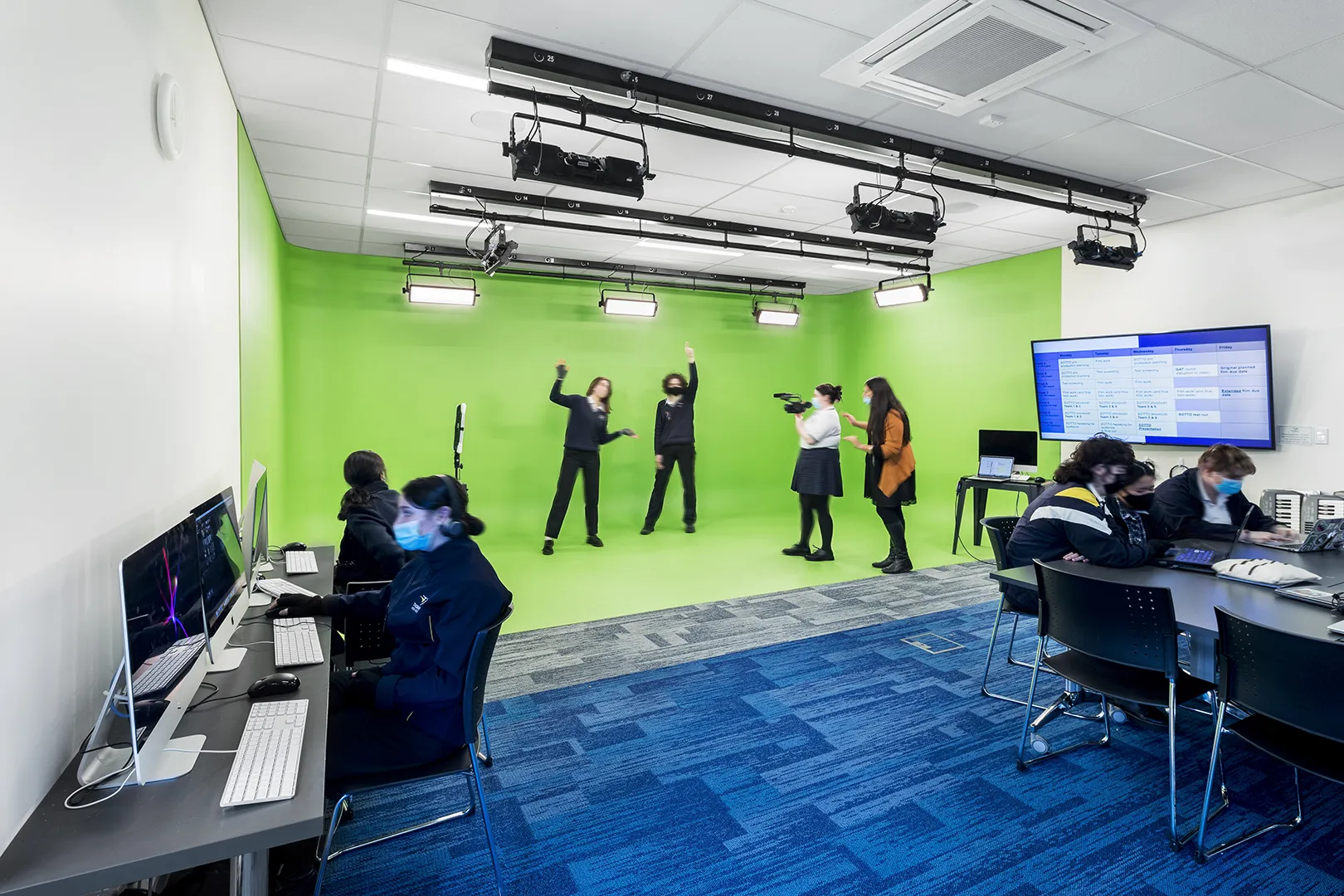 Students learning in a media production studio with video equipment, computers, and a green screen for digital content creation.