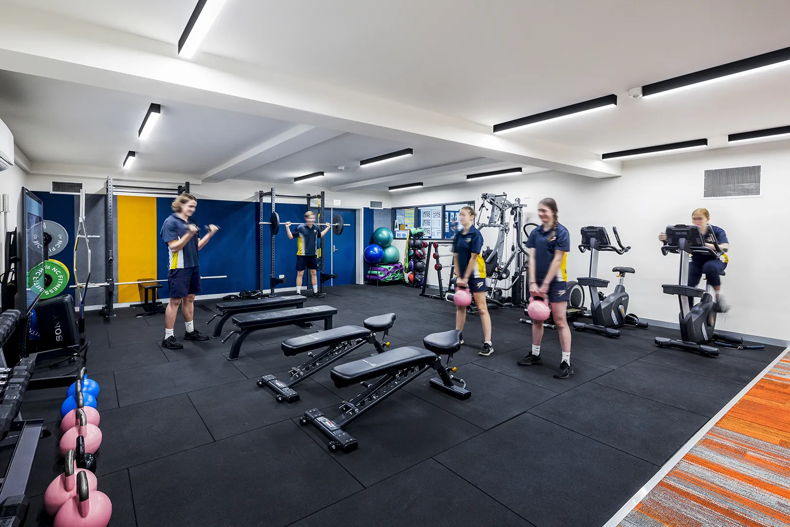 Students using a fitness and training space equipped with weights, exercise machines, and areas for physical education activities.