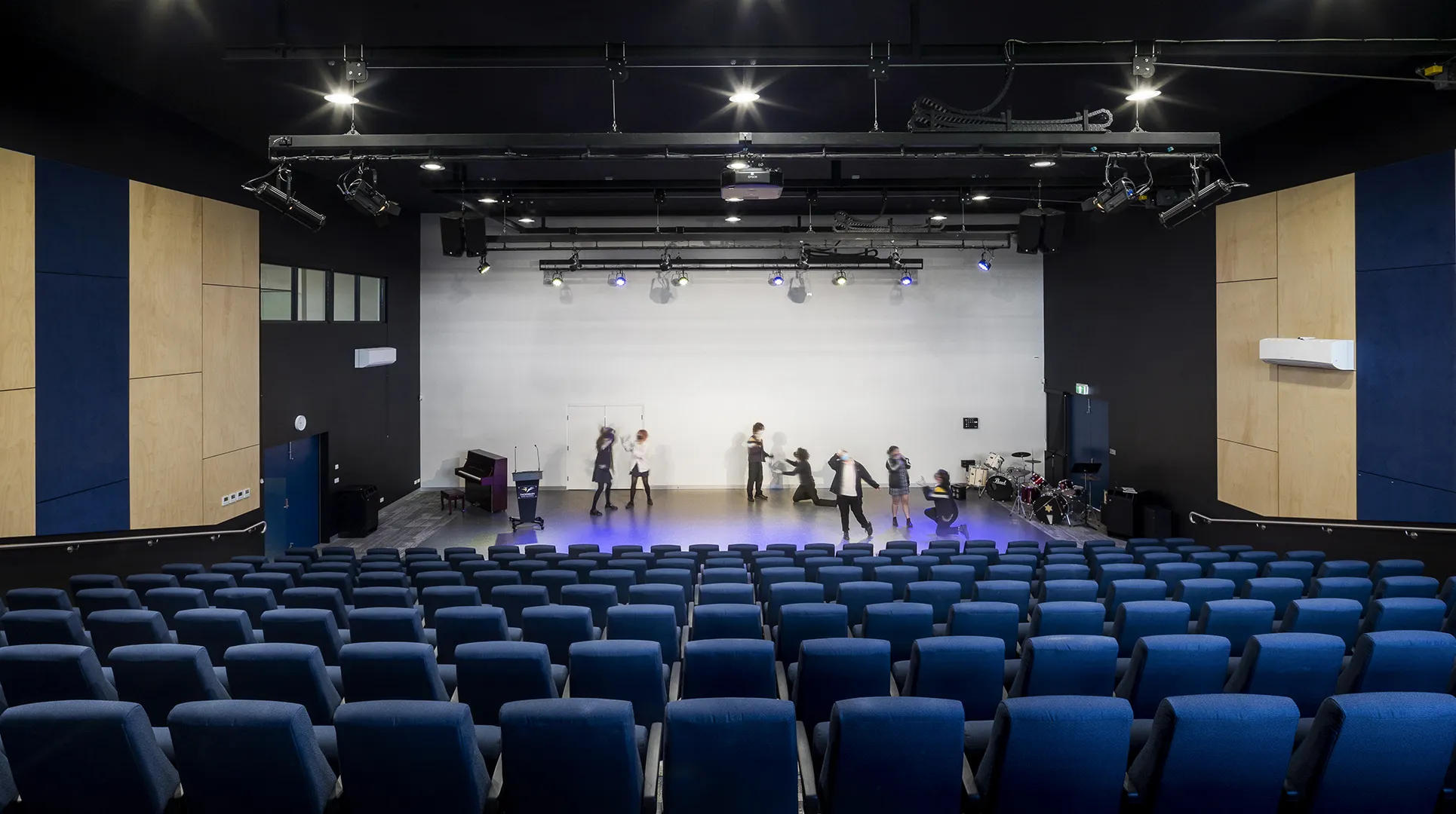 School theatre with tiered seating, stage lighting, and students using a performing arts space for presentations and rehearsals.
